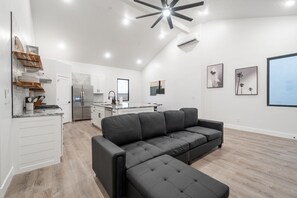 A modern kitchen with white cabinets, a black sofa, and a large window.