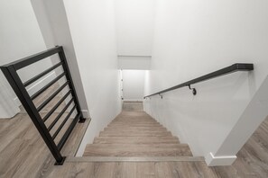 Eine Treppe mit Holzdielen und schwarzen Metallgeländern, die zu einem Raum mit weißen Wänden und einer Tür oben führt.