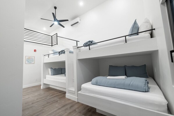 Ein moderner, gut beleuchteter Raum mit Etagenbetten, einem Deckenventilator und einem gerahmten Bild an der Wand.