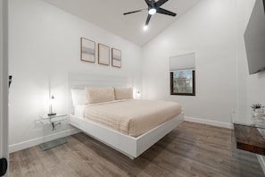 Een moderne slaapkamer met een bed, nachtkastjes, een plafondventilator en lijstwerken aan de muur.