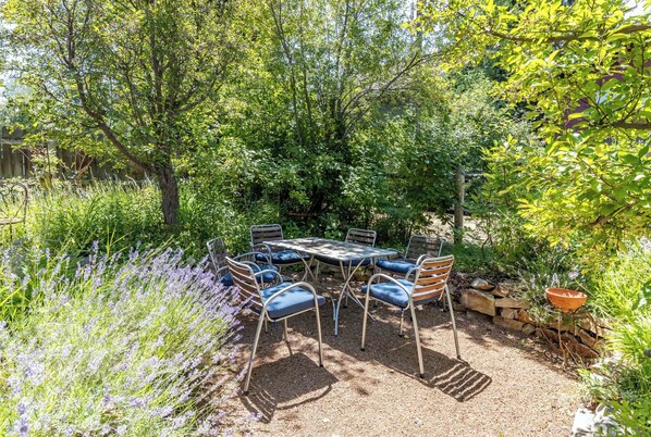 An outdoor patio with a metal table and chairs, surrounded by lush greenery and lavender plants. - Charming Ketchum Cottage with Gourmet Kitchen (Ketchum)