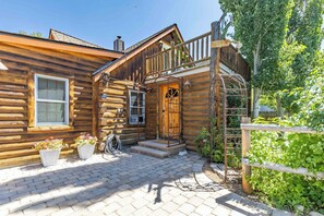 A rustic log cabin with a wooden porch, a stone staircase, and potted flowers. - Charming Ketchum Cottage with Gourmet Kitchen (Ketchum)
