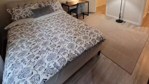 A bedroom with a bed, a desk, a lamp, and a door leading to a bathroom.