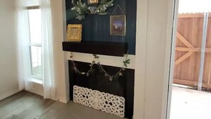 A room with a fireplace, a window with white curtains, and a wooden fence outside.