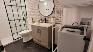 A modern bathroom with a hexagonal tile floor, a toilet, a sink with a mirror, and a washing machine.