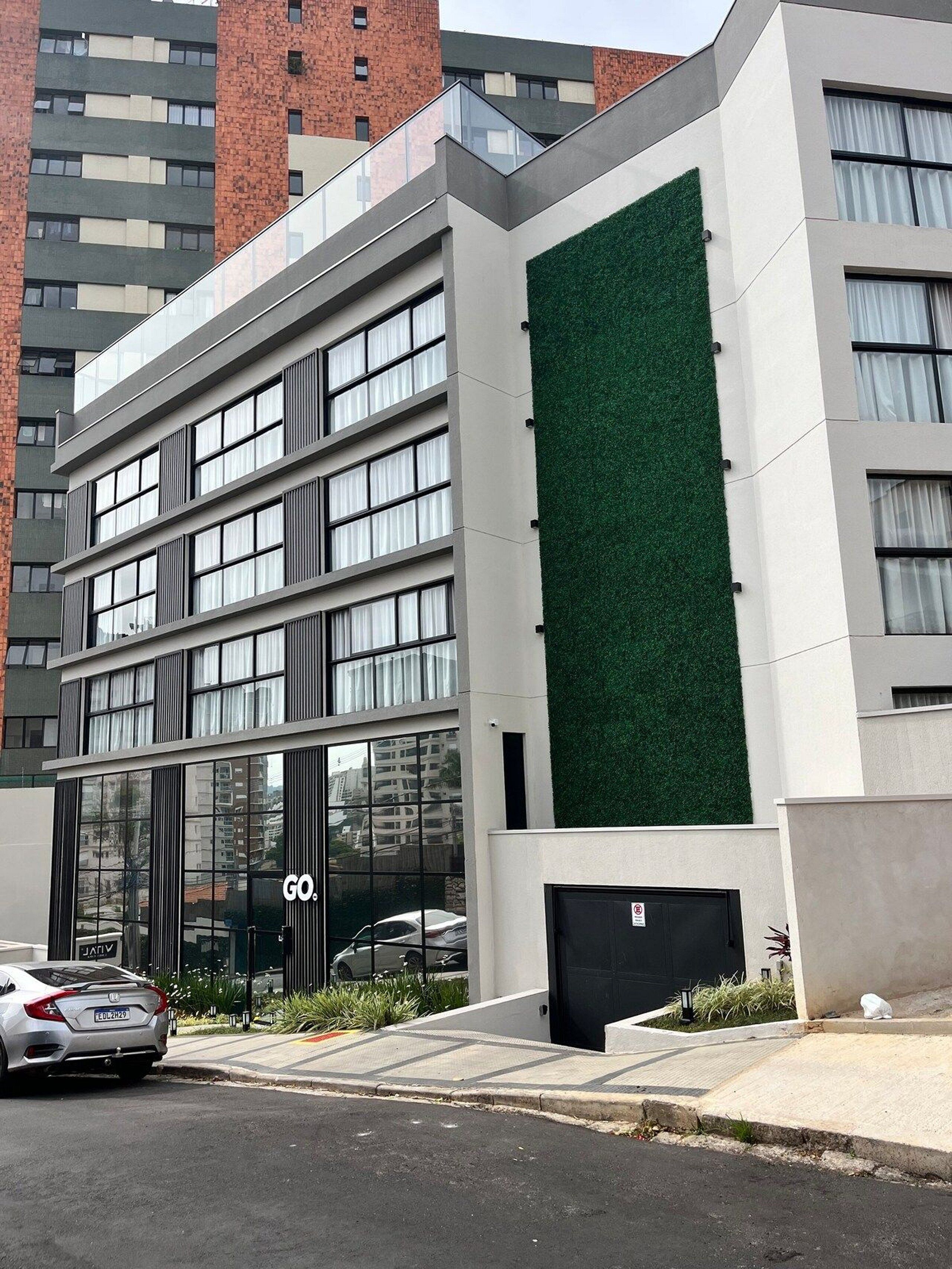 A modern building with a glass facade, a green vertical garden, and a car parked in front.