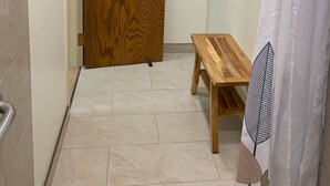 Un baño con puerta de madera, cortina de ducha, toallero y banco de madera.