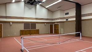 Una cancha de tenis con red, paneles de madera y un aro de baloncesto.
