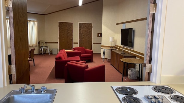 Habitación de hotel con kitchenette, un sofá rojo, televisor y una mesita de noche con lámpara.