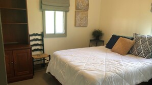 A bedroom with a large bed, a wooden wardrobe, a chair, a window with blinds, and a small side table with a plant. - Charming farmhouse property on 20 acres of land, comfortably sleeps 13   (Lava Hot Springs)