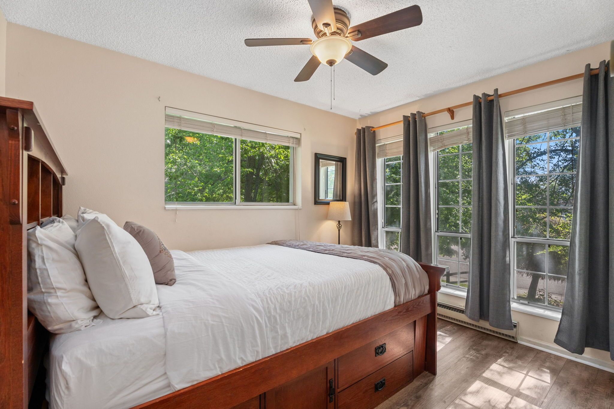 A bedroom with a bed, a ceiling fan, a window with curtains, and a view of trees.