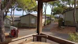 A covered outdoor area with a wooden table and chairs, surrounded by trees and a view of beach cottages. - Logement Entier : Cabane - Agde, France (Agde)