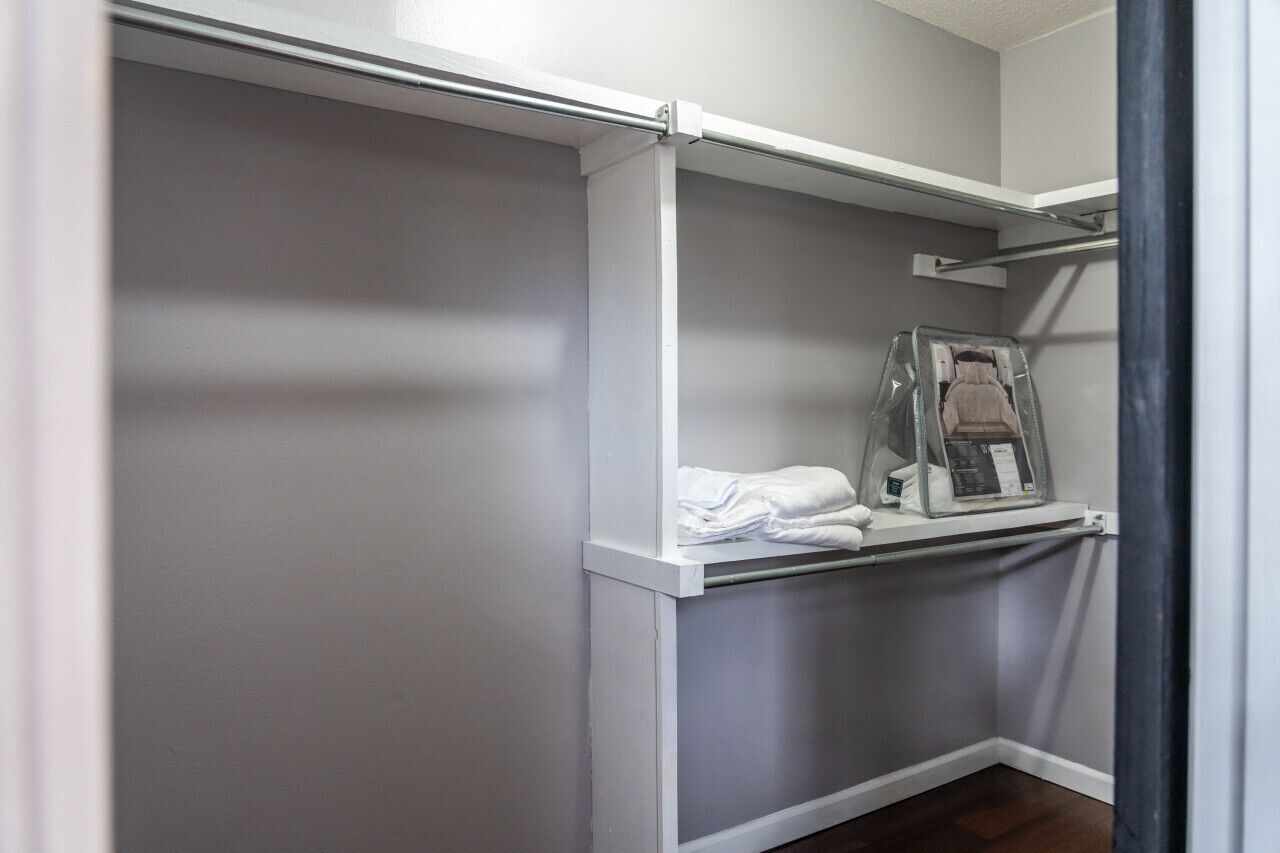 A walk-in closet with a white door, a hanging rod, and a shelf with folded clothes.