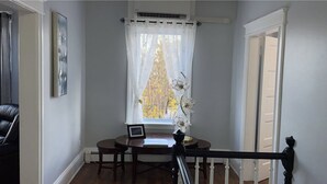 A corner room with a window, a table with a chair, a picture frame, and a staircase railing. - Newly renovated 2 bedroom apartment  (Saint John)