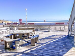 Eine Holzterrasse mit Bänken und Tischen, mit Blick auf einen Strand und einen klaren Himmel.