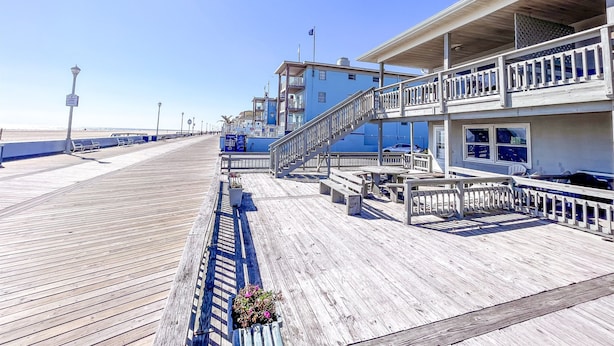 A wooden boardwalk leading to a beachfront building with a balcony and a staircase. - Oceanfront Boardwalk Condo Patio (Ocean City)