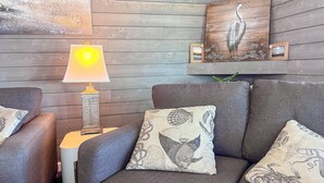 A cozy seating area with grey sofas and patterned cushions, a wooden wall, and a lamp. - Oceanfront Boardwalk Condo Patio (Ocean City)