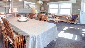 A dining area with a table set for four, surrounded by wooden chairs. There are hanging pendant lights above the table. - Oceanfront Boardwalk Condo Patio (Ocean City)