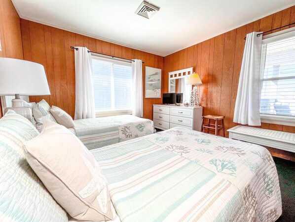 A bedroom with two beds, a dresser, a chair, a desk, and a window with curtains. - Boardwalk Condo with Ocean Views (Ocean City)