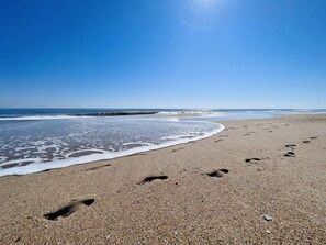 A beach with footprints leading to the water, a clear sky, and waves approaching the shore. - Boardwalk Condo with Ocean Views (Ocean City)