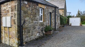 A stone building with a gravel driveway, a chimney, and a white garage door. - 1 bedroom accommodation in Lesbury Near Alnwick (Lesbury Near Alnwick)