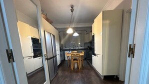 Een smalle gang met houten vloeren die leidt naar een keuken met witte kasten en een eettafel met stoelen.