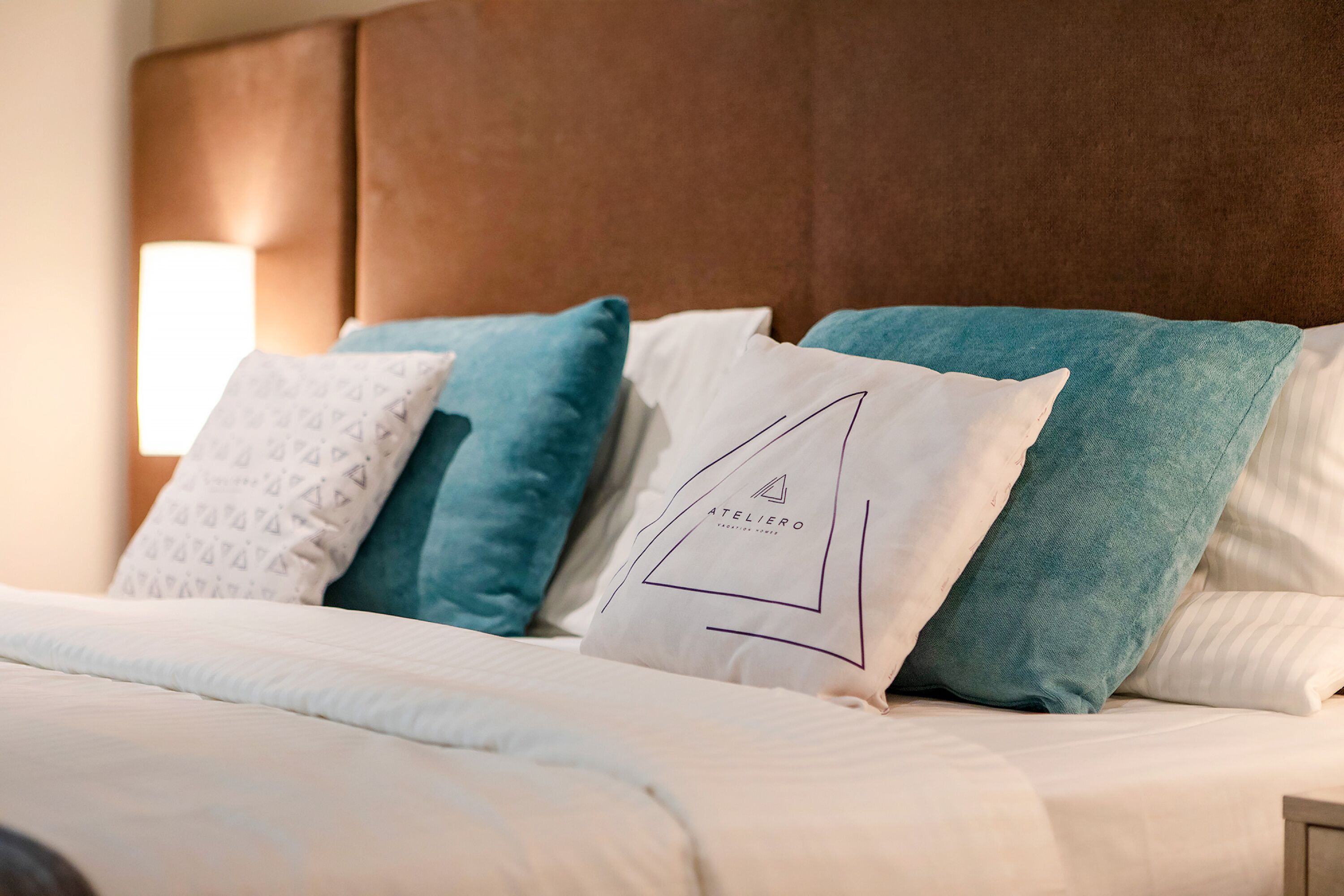 A neatly made bed with a white comforter and multiple pillows, including a pillow with a geometric design and another with a logo.