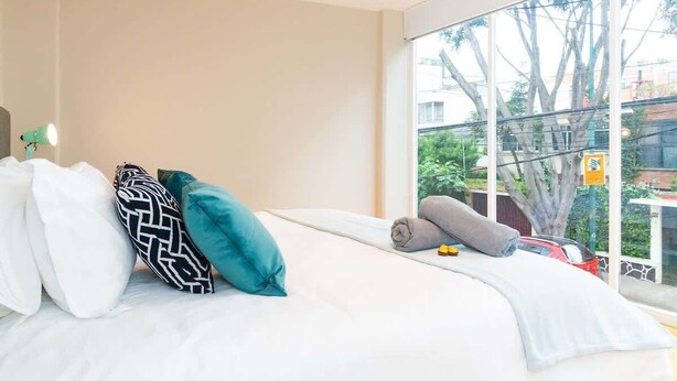 Ein Schlafzimmer mit Bett, Kissen, einem Fenster und Blick ins Freie.