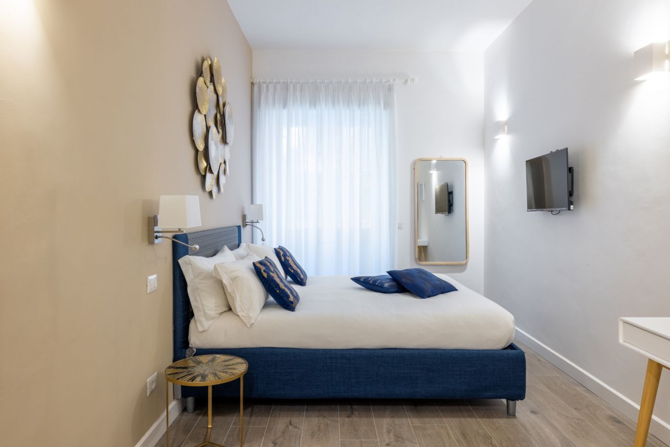 A bedroom with a bed, bedside tables, a TV, and a mirror on the wall.