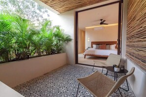 A balcony with patterned flooring, a wicker chair, and a bed with a wooden headboard visible through an open door. - Nature Retreat: Tulum Apartment with Tub & Terrace (Tulum)