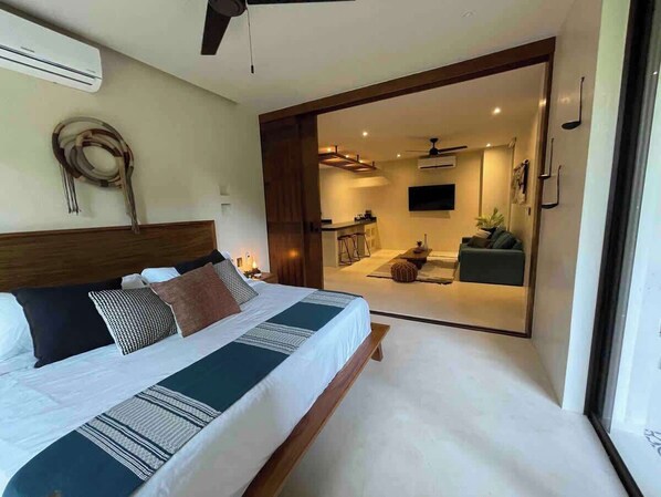 Un dormitorio con una cama grande, cabecera de madera y vistas a un comedor por una puerta abierta.
