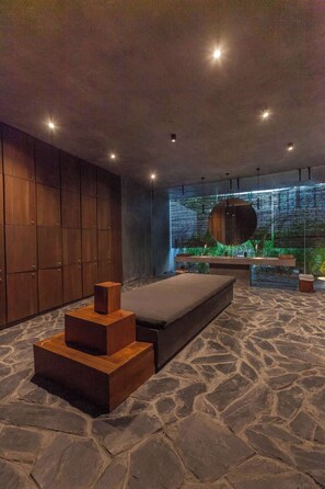 A modern bedroom with a stone floor, a bed, a wooden bench, and a wall with a vertical garden.