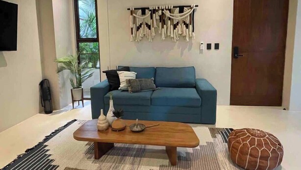 A modern living room with a blue sofa, a wooden coffee table, and a macrame wall hanging.