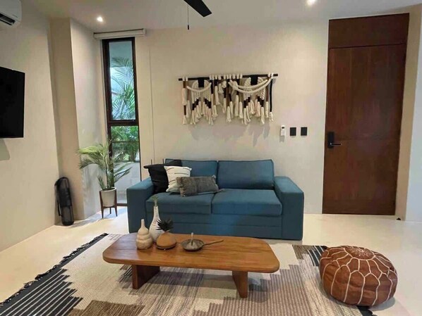 A modern living room with a blue sofa, a wooden coffee table, and a macrame wall hanging.