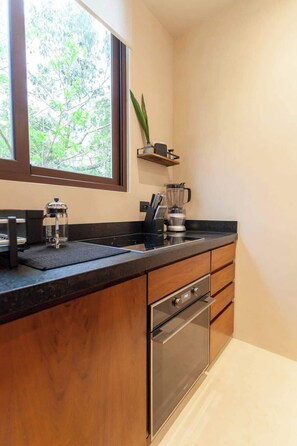 A modern kitchen with a built-in oven, a coffee maker, and a window with a view of trees. - Nature Retreat: Tulum Apartment with Tub & Terrace (Tulum)