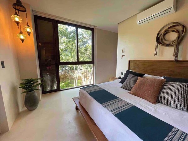 A bedroom with a large bed, a potted plant, and a view of greenery through a sliding door. - Nature Retreat: Tulum Apartment with Tub & Terrace (Tulum)