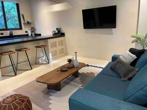 A modern living room with a sofa, a coffee table, and a kitchen area with stools. - Nature Retreat: Tulum Apartment with Tub & Terrace (Tulum)