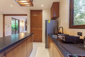 A modern kitchen with wooden cabinets, a stainless steel refrigerator, and a large window. - Nature Retreat: Tulum Apartment with Tub & Terrace (Tulum)