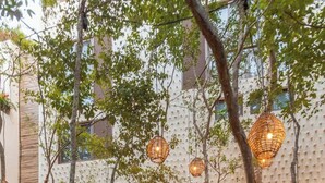 A pathway leading to a building with a textured wall and hanging wicker lamps.