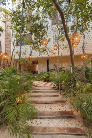 A pathway leading to a building with a textured wall and hanging wicker lamps. - Nature Retreat: Tulum Apartment with Tub & Terrace (Tulum)