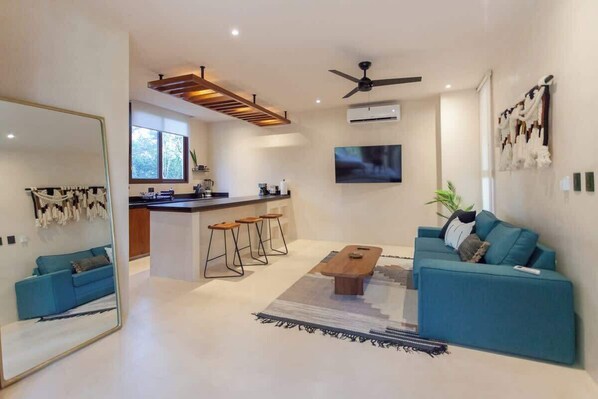 A modern living room with a blue sofa, a wooden coffee table, and a large mirror. - Nature Retreat: Tulum Apartment with Tub & Terrace (Tulum)
