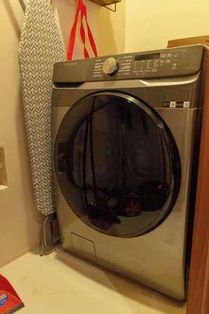 A front-loading washing machine in a laundry room with a patterned towel hanging on a rack.