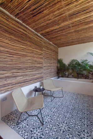 A covered outdoor seating area with two chairs and a small table, surrounded by patterned tiles and plants. - Nature Retreat: Tulum Apartment with Tub & Terrace (Tulum)