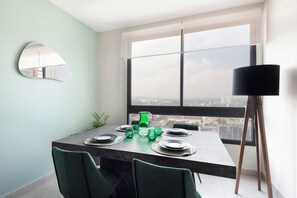 A dining area with a table set for four, a large window with a city view, a floor lamp, and a green plant.