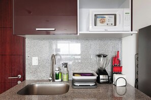 A kitchen with a stainless steel sink, a microwave, a blender, and various kitchen utensils.