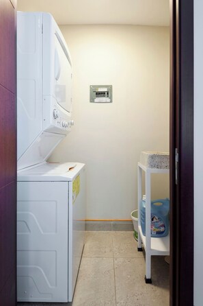 A laundry room with a white washer and dryer, a utility panel, and a shelf with cleaning supplies. - Beautiful design in Polanco, 2 rooms (Ciudad de México)