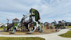Une aire de jeux dotée de plusieurs toboggans et de structures d’escalade, entourée d’un chemin pavé et de zones herbeuses.