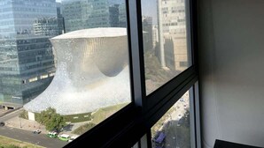 Une vue d’un bâtiment moderne à l’architecture originale, caractérisée par une structure incurvée, telle qu’elle appara ît à travers une fenêtre.