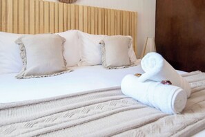 Un lit avec une literie et des oreillers blancs, une serviette enroulée et une tête de lit en bois.