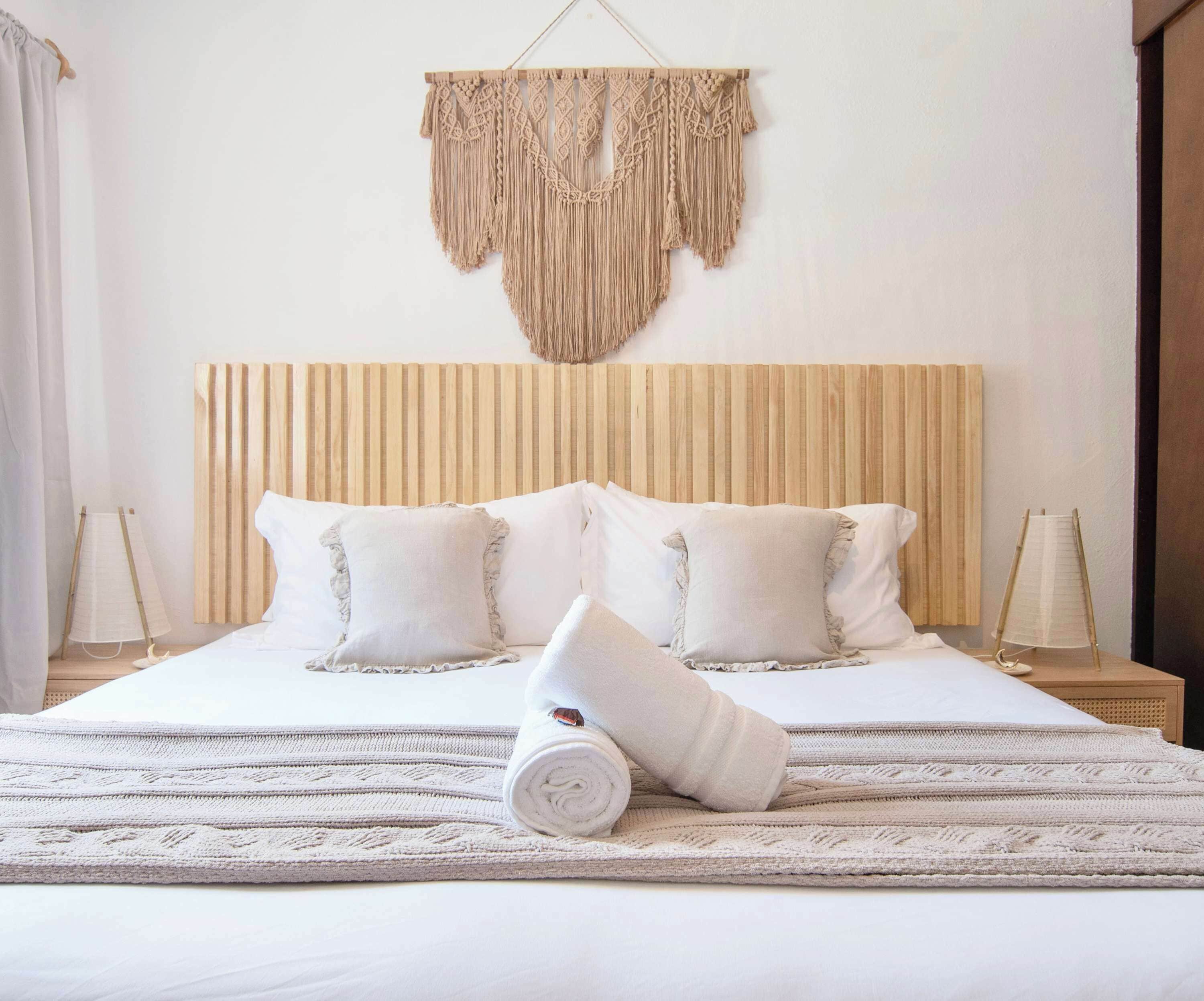 A hotel room with a wooden headboard, white bedding, and a macramé wall hanging.